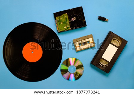 A collection of old and modern storage devices technology, Gramophone record videocassette audiocassette tape compact disk hard disk and flash drive on blue background