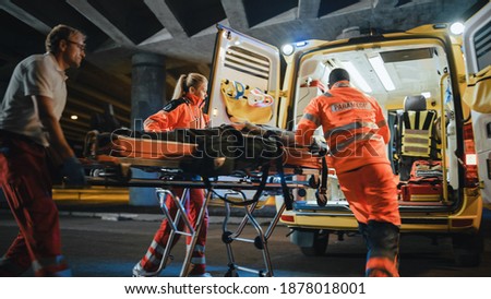 Team of EMS Paramedics React Quick to Provide Medical Help to Injured Patient and Get Him in Ambulance on a Stretcher. Emergency Care Assistants Arrived on the Scene of a Traffic Accident on a Street. Blurry Royalty-Free Stock Photo #1878018001