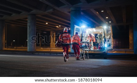 Team of EMS Paramedics React Quick to Provide Medical Help to Injured Patient and Get Him in Ambulance on a Stretcher. Emergency Care Assistants Arrived on the Scene of a Traffic Accident on a Street. Blur Royalty-Free Stock Photo #1878018094