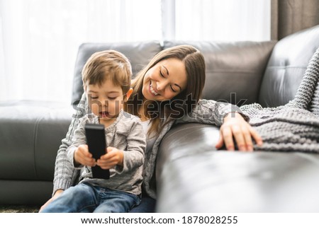 A Mother and her son are watching tv while sitting on a couch