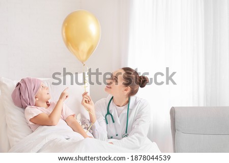 Doctor with golden balloon and little girl undergoing course of chemotherapy in clinic. Childhood cancer awareness concept Royalty-Free Stock Photo #1878044539