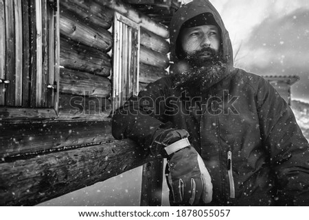 Bearded man in winter, adventure mountain man with a beard in the snow. Background of the old village