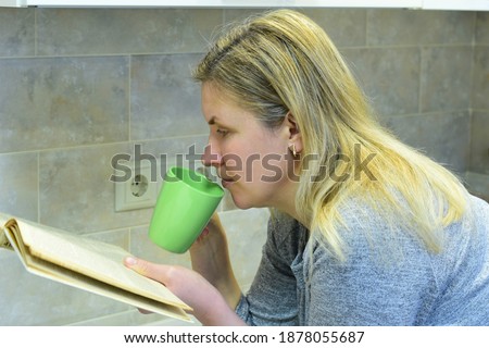 Leaning on the table, a woman drinks tea and reads a book.. High quality photo