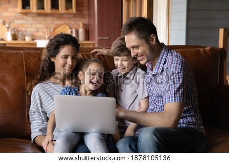 Funny movie. Friendly family with daughter son relax hug together on cozy couch on weekend use laptop. Laughing mom dad with two little children watch video online chat with grand parents by internet