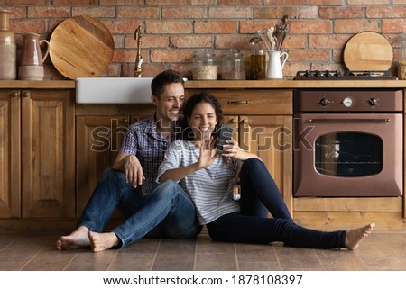 Selfie at new dwelling. Loving spouses first time buyers of modern house hugging on warm floor at kitchen satisfied of cozy home. Young husband and wife posing for self picture on cellphone indoors