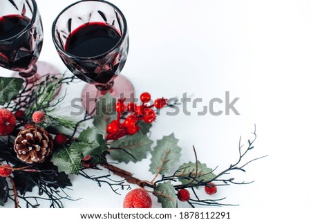glasses with red wine on a white background and a Christmas branch with berries . serving the festive table