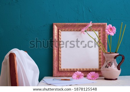 gerbera in an old vase, set for writing, photo frame on a blue background on the table