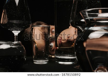 surreal portrait of a strange man looking through a magnifying glass and glasses of water on a black background