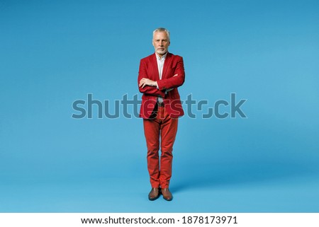 Full length of serious elderly gray-haired mustache bearded business man wearing red jacket suit standing holding hands crossed looking camera isolated on blue color wall background studio portrait Royalty-Free Stock Photo #1878173971