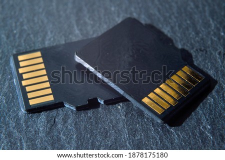 two micro sd cards lie on top of each other on a dark textured background, with golden contacts at the top. close-up.