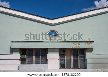 The facade of an old abandoned industrial building with broken dirty Windows and a corner roof on a blue sky background