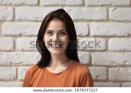Active life position. Headshot portrait of happy millennial woman posing by brick wall on background. Profile picture of young lady looking at camera with smile representing self motivation optimism.