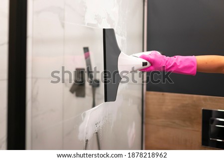 Female washes shower glass with electric glass cleaner. Professional bathroom cleaning process Royalty-Free Stock Photo #1878218962