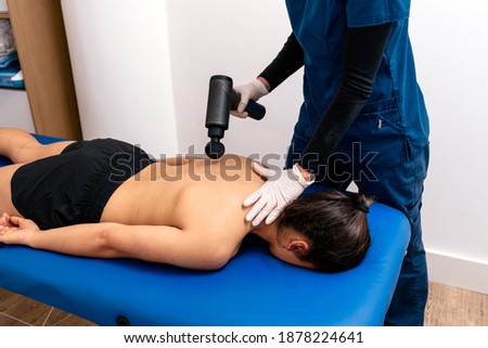 Stock photo of professional worker in physiotherapy clinic using electric massager with patient.