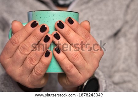 Woman's hands with black nail polish nails, silver fleece sweater, holding hot drink green or mug, tea cup beverage for cold winter days warmth, hygge style. Soft focus background.