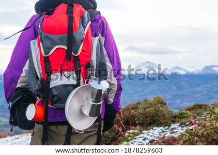 detail of an unrecognizable camper's backpack. red backpack with camping utensils in the background a landscape of snowy mountains.