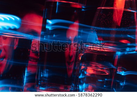psychedelic portrait of a mad psychopath male schizophrenic through glasses of water with blur and red blue neon lights Royalty-Free Stock Photo #1878362290