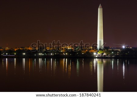 Washington Monument at night with city skyline on background. Colorful reflections in water of Tidal Basin.