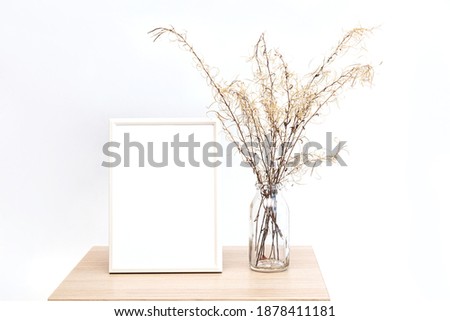 Mock up of a white photo frame in a minimalistic interior with a bouquet of pampas grass in a glass vase against a white wall background
