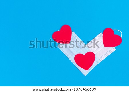 Valentine's symbol 2021. Heart shape of two medical protective masks and three red hearts on a blue background, copy space, flat lay, top view
