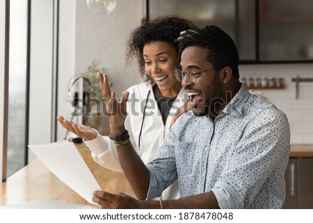 Happy young African American couple feel euphoric read good unbelievable news in paper letter correspondence. Overjoyed biracial man and woman triumph get pleasant message in paperwork. Royalty-Free Stock Photo #1878478048