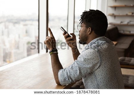 Back view of African American man record audio message on modern cellphone gadget. Young biracial male activated digital virtual voice assistant on smartphone. Communication, technology concept.