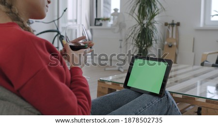 Woman holding tablet computer with green screen while watching something. Chroma key. Female having glass of wine while chatting with friend or partner online. Stay home, quarantine concepte