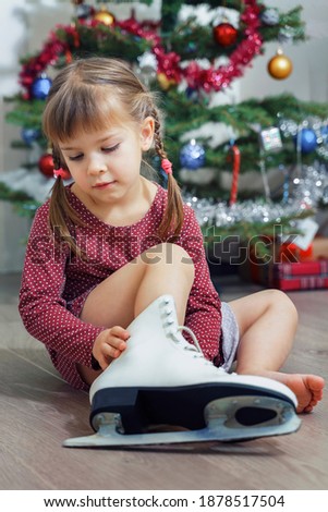 sad little girl trying on her mother's skates while sitting at home by the Christmas tree. restrictions due to the coronavirus epidemic. the child cannot leave the house. quarantine