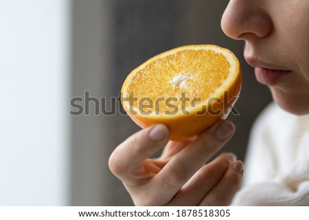 Sick woman trying to sense smell of  half fresh orange, has symptoms of Covid-19, corona virus infection - loss of smell and taste. One of the main signs of the disease.  Royalty-Free Stock Photo #1878518305