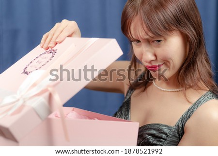 cute young brown-haired girl disappointed with a gift in a pink box on a blue background