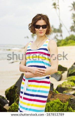 Beautiful young woman in sunglasses posing on the empty beach at coastline of Sri Lanka, Ceylon. Vertical image