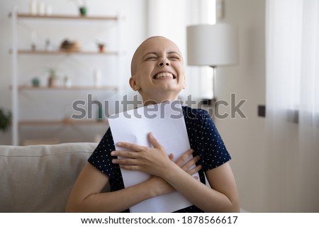 Excited young woman fighting against oncology scream in delight clasp document with good test result to chest. Happy sick lady laugh thank god hold paper letter medical conclusion that cancer receded. Royalty-Free Stock Photo #1878566617