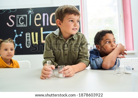 Waist up portrait of the three multiracial pupils sitting at the chemistry lesson and looking aside while listening their teacher. Education and science concept. Stock photo