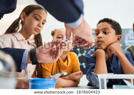 Cropped view of adult teacher showing test glass to his surprised pupils at the chemistry lesson at the school. Stock photo. Children, science and education concept
