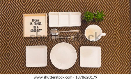 Top view of empty plates, positive signage, a mug, 2 plants, fork and spoon on a table. 