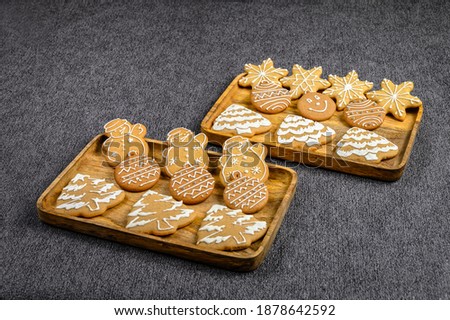 Christmas ginger cookies in the shape of snowmen, fir trees and stars in the rectangular wooden plates on a gray background. The view from the top.