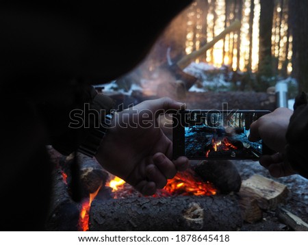 A man with a watch on his hands takes pictures on a modern mobile phone of a burning bonfire in nature. Photo in smartphone photos. The concept of accessible photography.