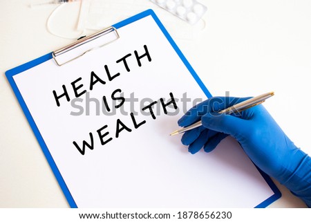 Female doctor's hand in a medical glove makes an inscription HEALTH IS WEALTH in a document.
