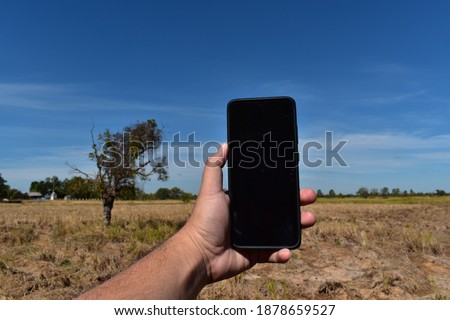 Mockup image of woman's hand holding black mobile phone with blank desktop screen by 
Rice fields with blue sky background. 
Global warming concept.