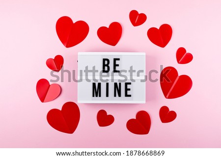 Red paper hearts and lightbox with text Be Mine on pink background. Valentine's day, love, anniversary concept