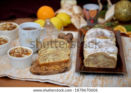 Home baked walnut babka, sweet bread swirl and buns in baking pot stuffed with walnuts; bread texture of sliced walnut roll on wooden board and plate; wheat potato bread loaf in background