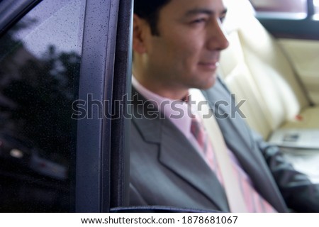 Close-up portrait of a smiling businessman sitting in the backseat of a car wearing a seatbelt.