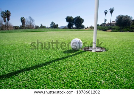 Close-up surface level picture of a golf ball at the edge of the hole on putting green.
