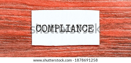 COMPLIANCE text on the piece of paper on the red wood background