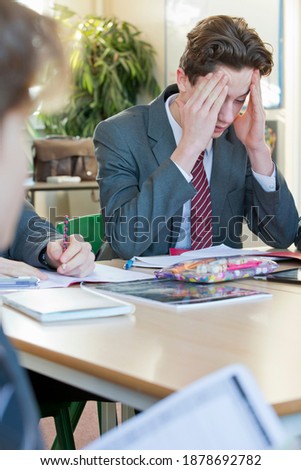 Vertical shot of a high school boy sitting with his hands on the head while completing his math homework.