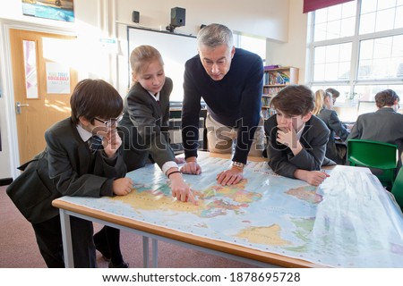 Geography teacher and middle school students using a map in the classroom. Royalty-Free Stock Photo #1878695728