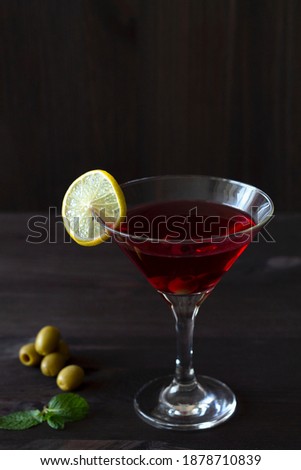 cosmopolitan cocktail. Martini glass with cocktail and olives on black background. Red cocktail with green mint and lime on the wooden table. copy space. alcohol drinks. vertical.