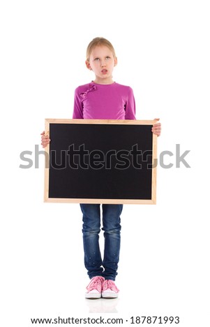 Grimacing schoolgirl standing with blackboard. Full length studio shot isolated on white.