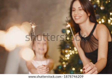 People reparing for Christmas. Mother playing with her daughter. Family is resting in a festive room. Little girl in a pink dress.