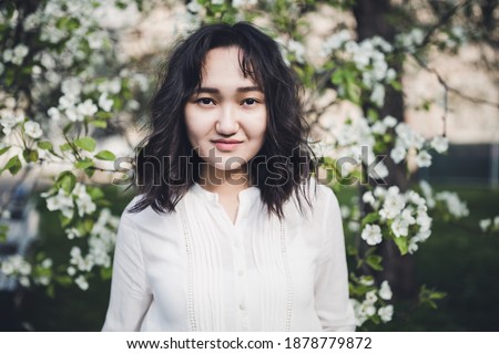 Young attractive asian woman in a white shirt under the blooming tree in park, calm, smiling. Spring portrait, lifestyle concept. Moody picture, copy space